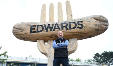 Ieuan Edwards poses with his arms crossed in front of a giant artificial fork with a giant artificial sausage with the word 'Edwards' engraved into it