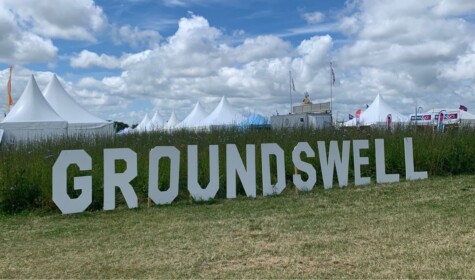 A sign for Groundswell sits on the grass at the site with tents displayed in the background