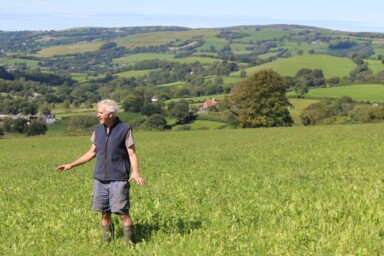 Patrick Holden stands alone in a grassy field amid a backdrop of farmland