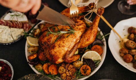 A roast chicken being carved on a plate alongside an assortment of vegetable side dishes
