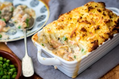 A rectangular dish of fish pie next to a bowl of peas. Courtesy of Getty images via canva