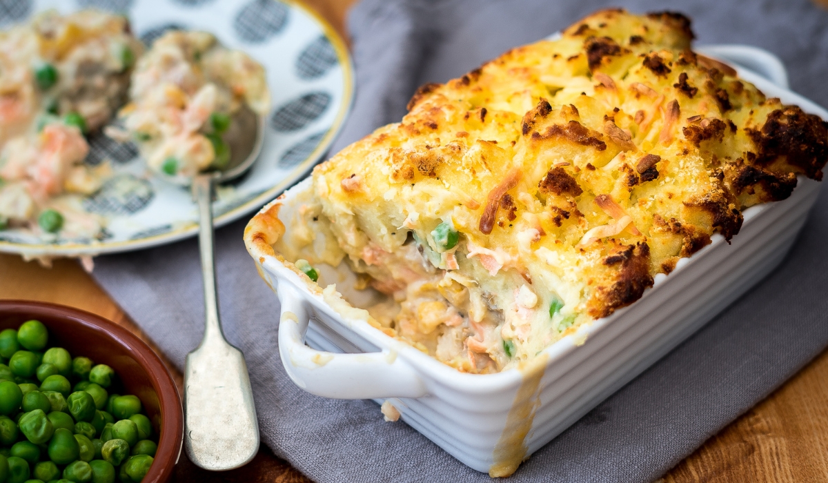 A rectangular dish of fish pie next to a bowl of peas. Courtesy of Getty images via canva